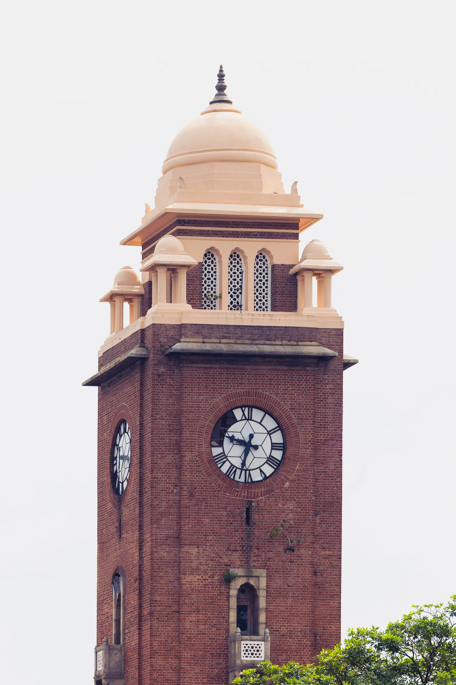 A red-brick clock tower with a cream dome, small domed pavilions at the corners and a large clock on its face, against a pale sky.