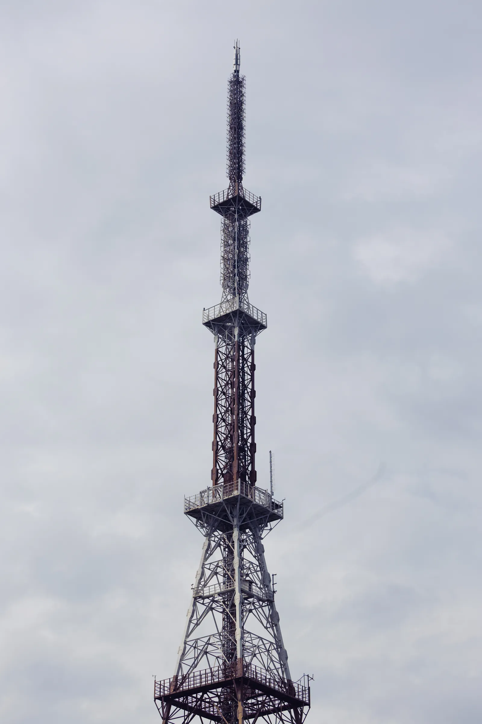 A tall steel-lattice radio tower with platforms and antennas, rising into an overcast grey sky.