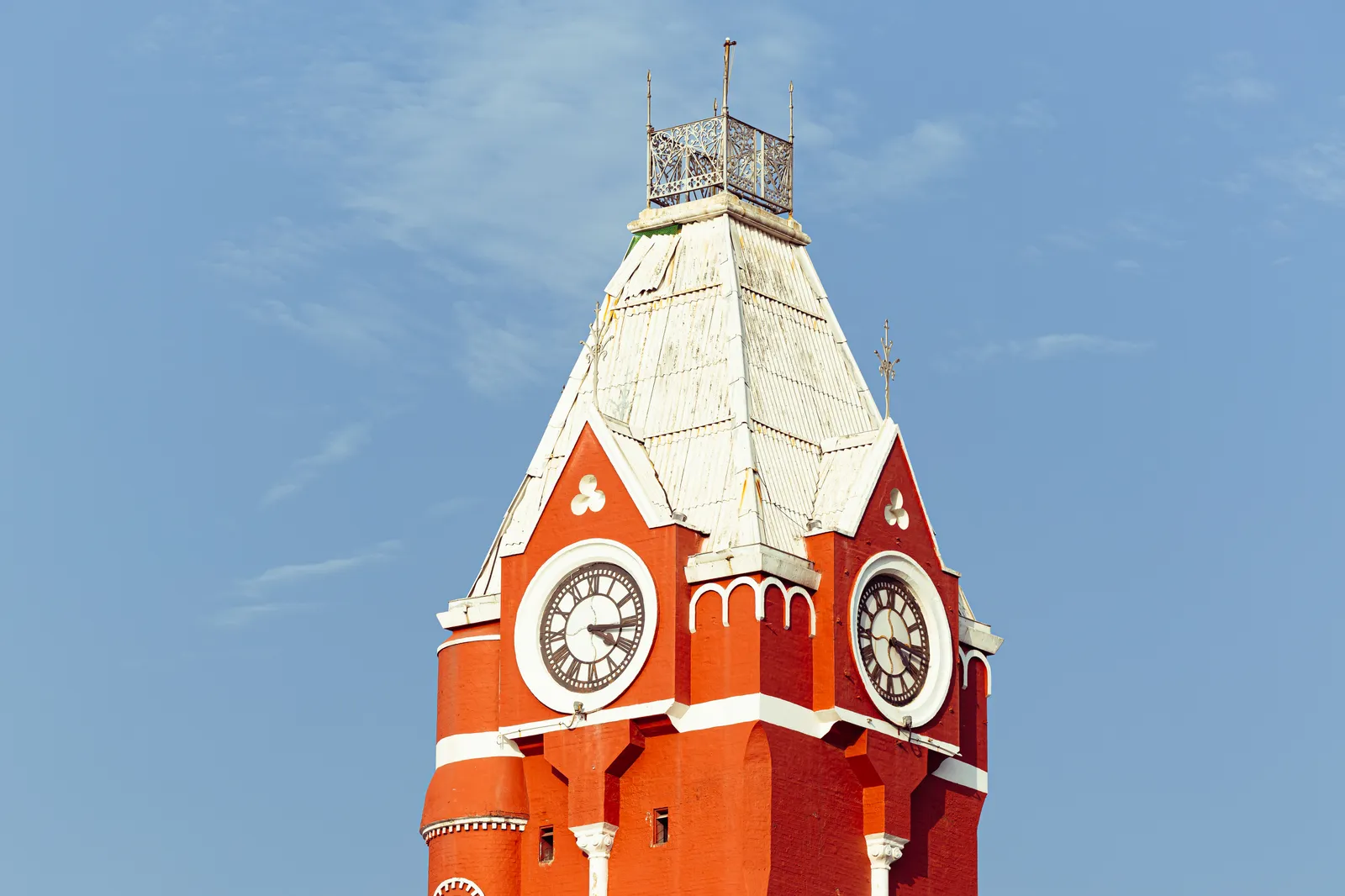 The red-and-white top of a clock tower with a pointed roof and two clock faces, against a clear blue sky.